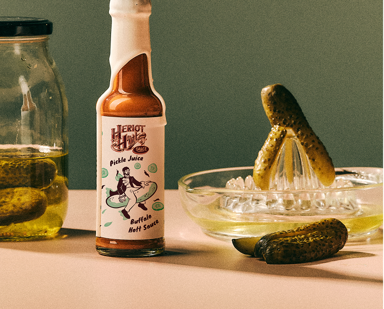 Pickle Juice Buffalo Hott Sauce with Jar of Pickles and a Pickle that has been Juiced- Heriot Hott